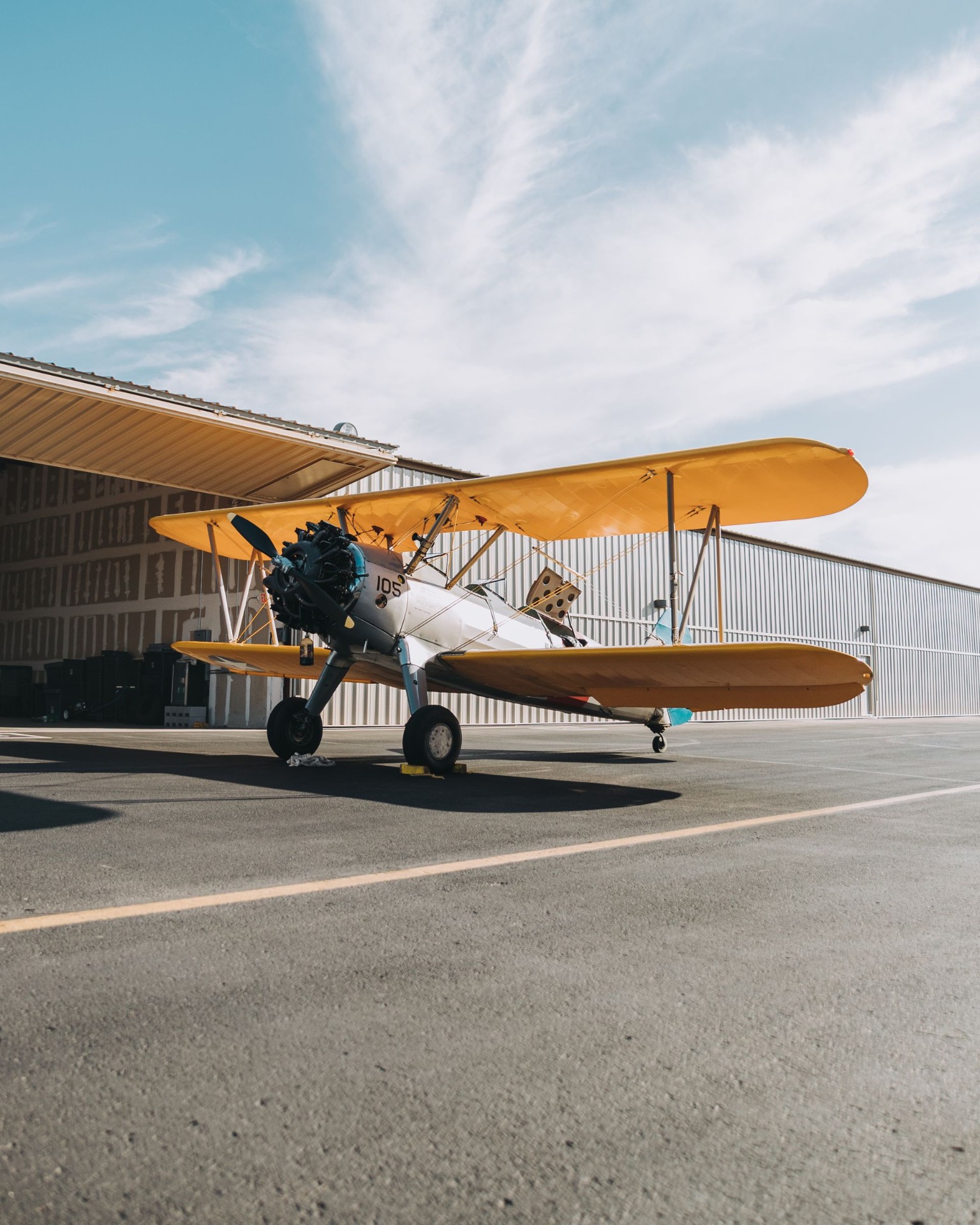 Vintage yellow biplane parked at a hangar